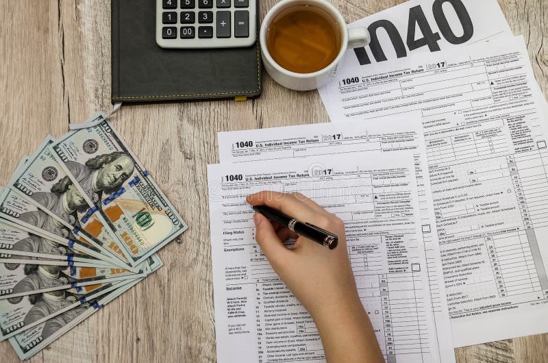 The female hand fills the tax forms 1040 on a wooden table stock photos The female hand fills the tax forms 1040 on a wooden table stock photos