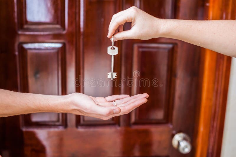 Female hand giving a key to the house a man`s hand on a background of a wooden door. Owning real estate concept