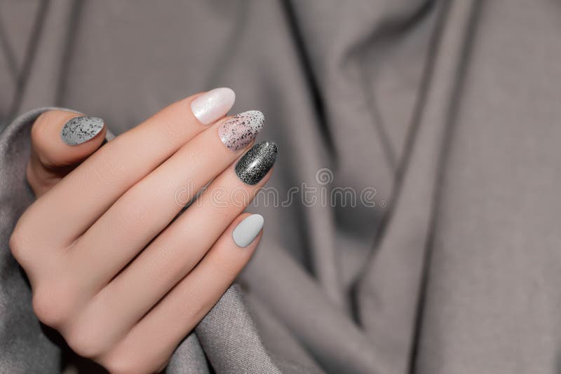 Female hand with glitter black nail design. Silver nail polish manicure. Woman hand on gray fabric