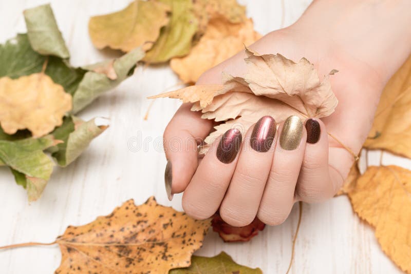 Female hand golden with nail design. Gold and red nail polish manicure. Woman hand hold yellow autumn leaf