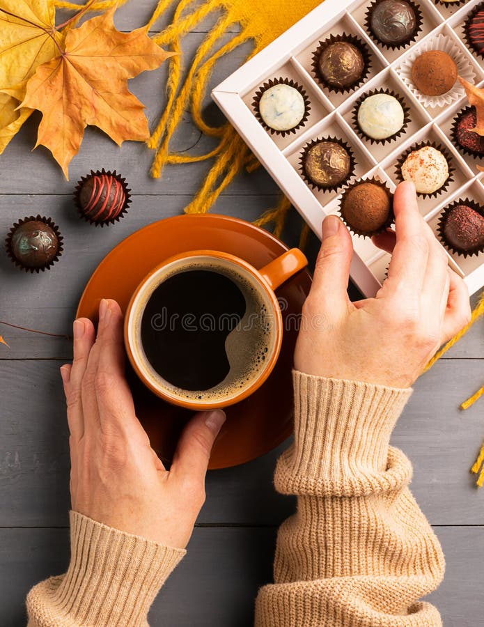 Female hand hold a cup of hot black coffee chocolate truffle orange scarf on autumn background. Top view flat mockup