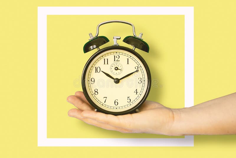 Female Hand Holding an Alarm Clock in a White Frame Against a Yellow  Background. Stock Image - Image of timer, table: 205186789