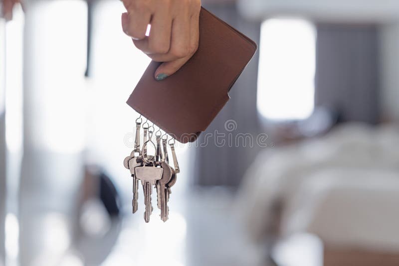 Female Asian hand holding brown leather key holder in bedroom