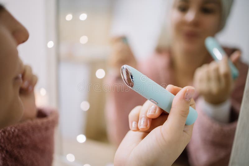 Female hand holding electric vibration eye massager. Woman`s hand holding anti-ageing wrinkle massager with blurred female reflection stock image Female hand holding electric vibration eye massager. Woman`s hand holding anti-ageing wrinkle massager with blurred female reflection stock image