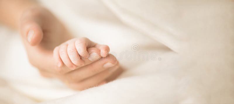 Female hand holding her newborn baby`s hand. Mom with her child. Maternity, family, birth concept. Copy space for your