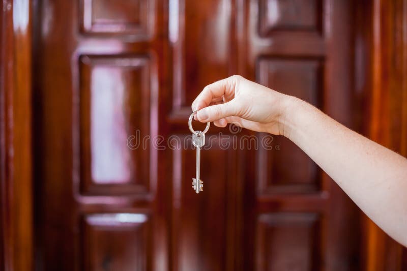 A female hand holding a key to the house on a background of a wooden door. Owning real estate concept stock images A female hand holding a key to the house on a background of a wooden door. Owning real estate concept stock images