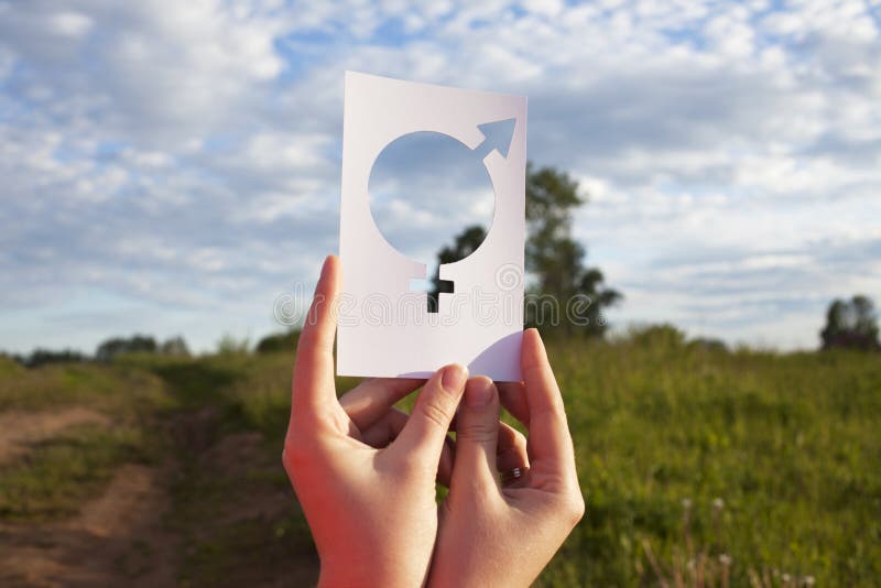 Female hand holding a symbol of gender equality against the background of blue sky with clouds. Nature stock photography Female hand holding a symbol of gender equality against the background of blue sky with clouds. Nature stock photography