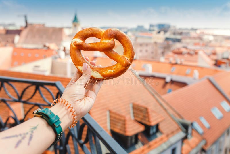 Ženská ruka drží tradiční pekařství preclíkovou pochoutku na pozadí historického centra evropského města