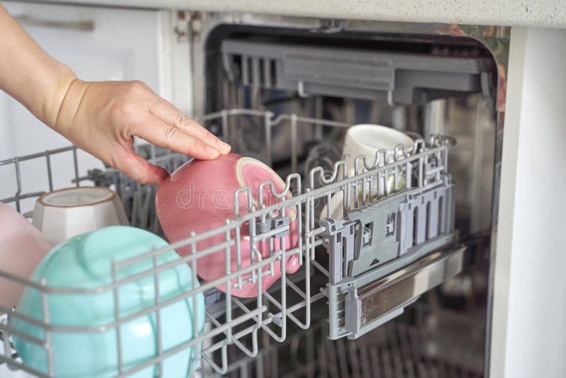 Female hand loading colorful ceramic mugs into dishwasher for cleaning and organization. Automatic loading stock images, royalty-free photos and pictures