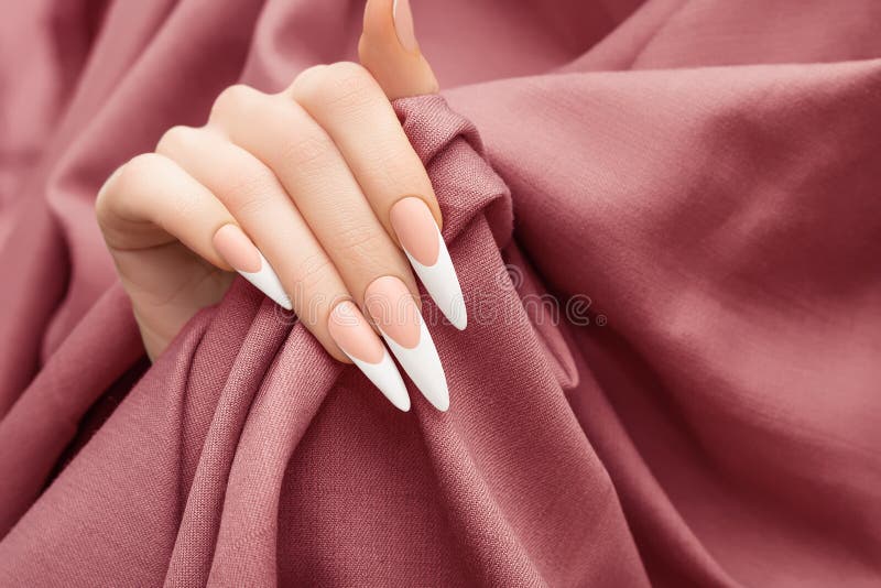 Female hand with long french nail design. Long french nail polish manicure. Woman hand on red fabric background