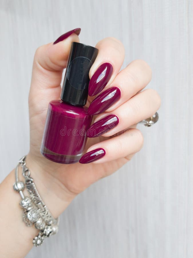 Female hand with long nails holds a bottle with a bordo nail polish. Female hand with long nails holds a bottle with a bordo nail polish