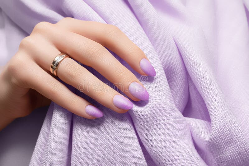 Female hand with purple nail design. Purple nail polish manicure. Woman hand on purple fabric background