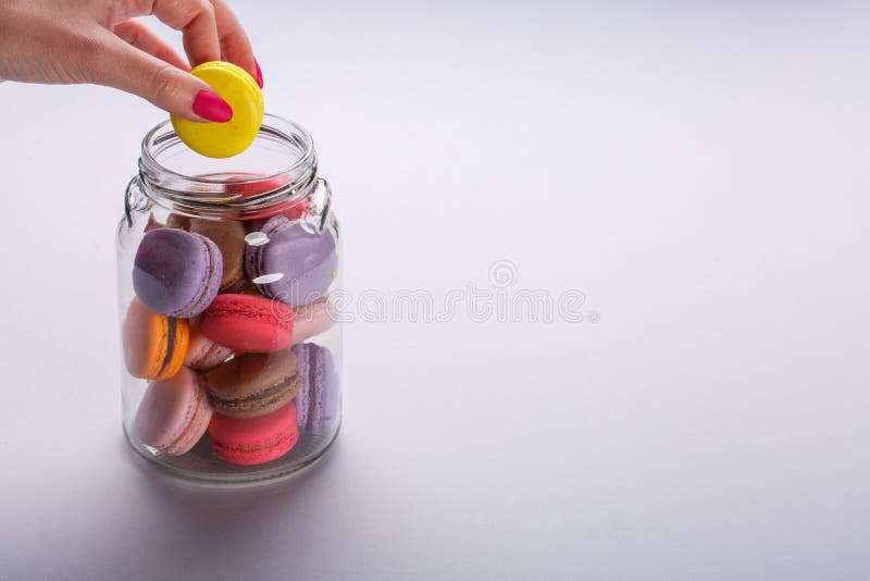 Female hand taking tasty colorful macaroons from glass jar on light gray background. Space for text stock photography Female hand taking tasty colorful macaroons from glass jar on light gray background. Space for text stock photography