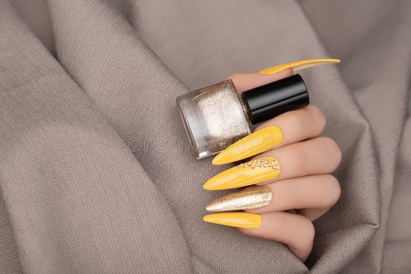 Female hand with yellow nail design. Long nail manicure. Woman hand with gold nail art hold gold nail polish bottle