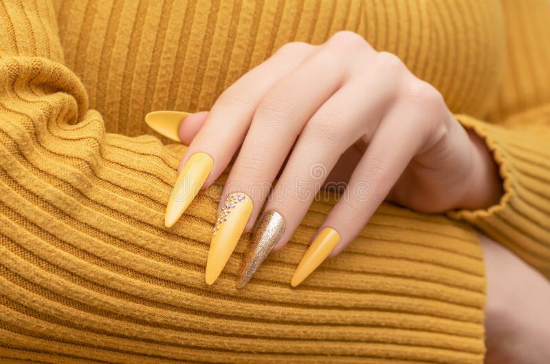 Female hand with yellow nail design. Long nail polish manicure. Woman manicure with gitter gold long nail art