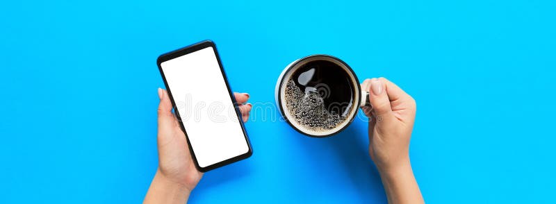 Female hands holding black mobile phone with blank white screen and mug of coffee. Mockup image with copy space for you design.