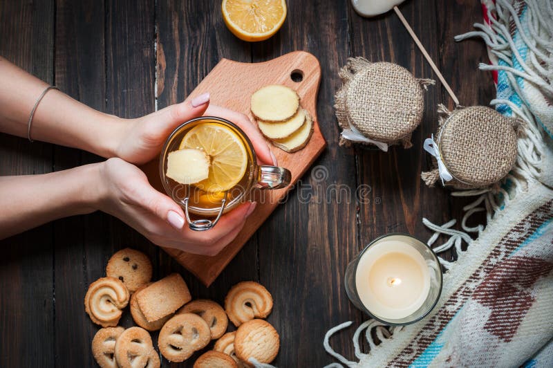 Female hands holding cup black tea with lemon, ginger and cookies on dark wood