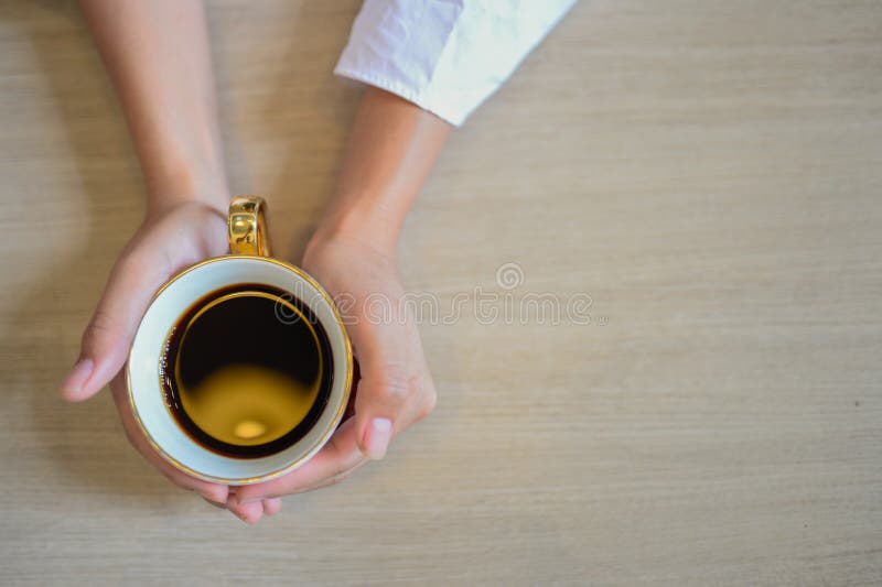 Female hands holding a cup of coffee with espresso coffee on wooden table