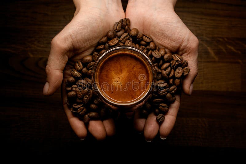 Female hands holding roasted coffee beans and cup of coffee over wooden surface