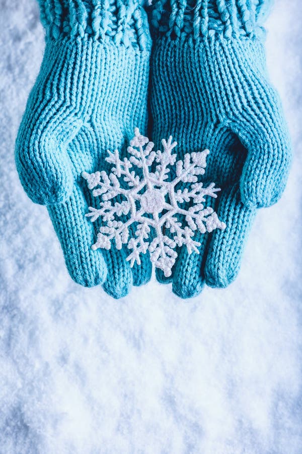 Female hands in light teal knitted mittens with sparkling wonderful snowflake on a white snow background. Winter Christmas concept