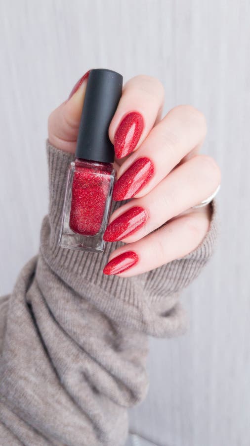 Female hands with long nails with red nail polish bottle