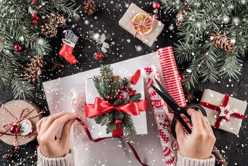 Female hands packs a Christmas gift box with red ribbon on holiday background with Fir branches, pine cones. stock photos Female hands packs a Christmas gift box with red ribbon on holiday background with Fir branches, pine cones. stock photos