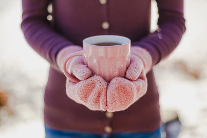 Female hands in pink mittens holding cup with hot tea or coffee. Close up