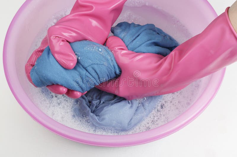 Female hands in rubber gloves wring out blue clothes on a background of a basin with linen close-up, top view