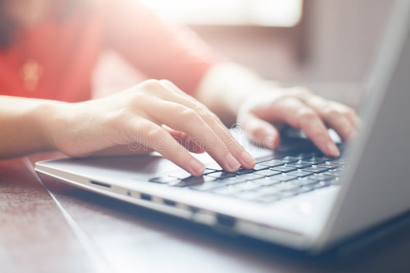 Female hands typing on keyboard of laptop surfing Internet and texting friends via social networks, sitting at wooden table indoor stock photo