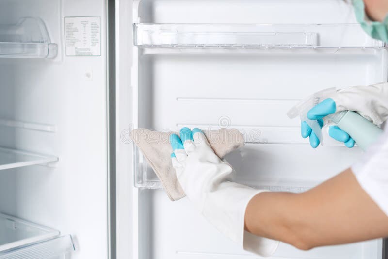 Female hands in white rubber glove clean empty refrigerator with spray bottle and rag in kitchen at home. Cleaning service