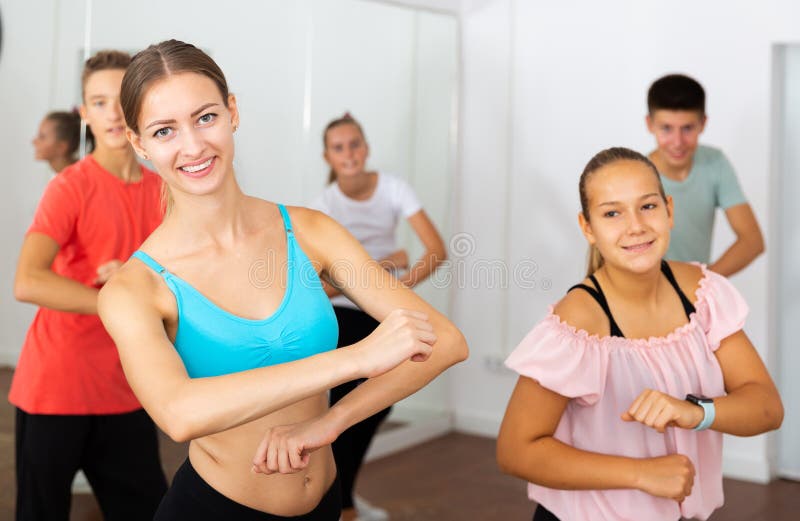 Portrait of young female instructor fulfilling dance movements with teenage boys and girls in modern studio. Portrait of young female instructor fulfilling dance movements with teenage boys and girls in modern studio