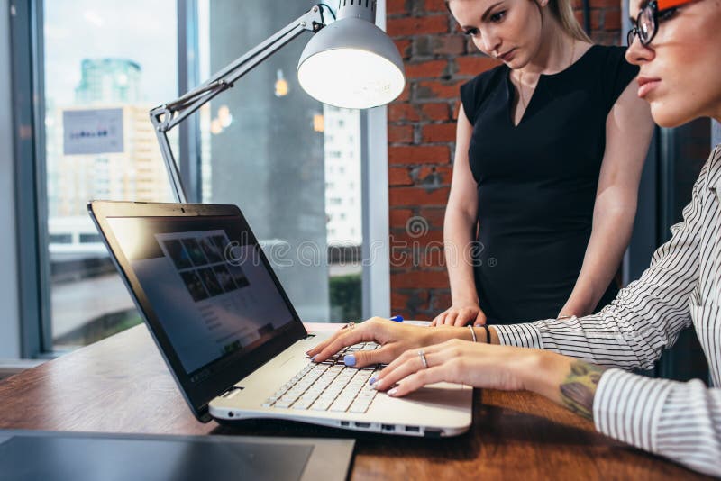 Female interior designer working with a customer watching pictures using laptop sitting at modern studio stock image