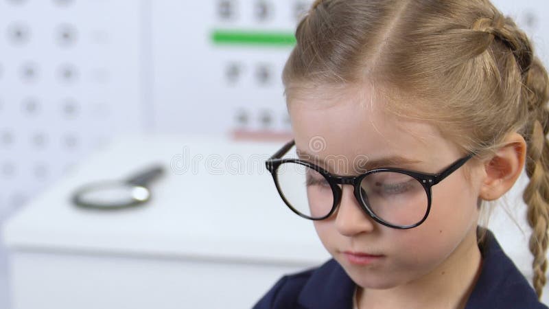 Female kid wearing eyeglasses prescribed by doctor, looking in mirror, frame