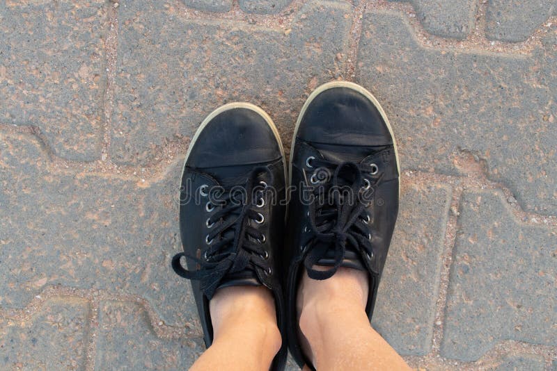 Female legs in black sneakers in summer stand on the road a view from the top close-up stock image Female legs in black sneakers in summer stand on the road a view from the top close-up stock image