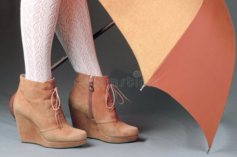 Female legs in brown suede boots under an umbrella on a gray background. Waterproof treatment for suede boots concept.