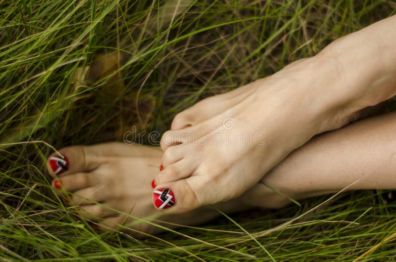 Female legs close-up, toes with a beautiful pedicure,. Feet and toes, female slender legs with a beautiful pedicure are resting barefoot on the green grass