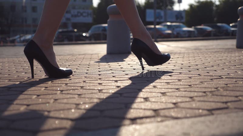 Female legs in high heels shoes walking in the urban street near auto parking. Business woman stepping to work. Young