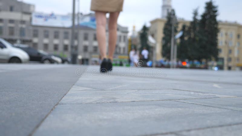 Female legs in high heels shoes walking in the urban street near the camera. Feet of young business woman in high-heeled