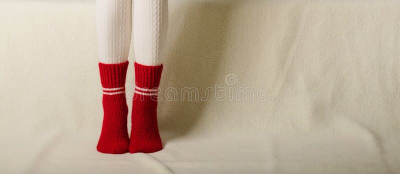 Female legs in warm white knitted tights and red socks on a whit