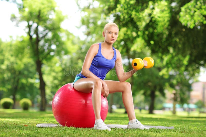 Female Lifting Weigth and Sitting on an Exercise Ball in Park Stock