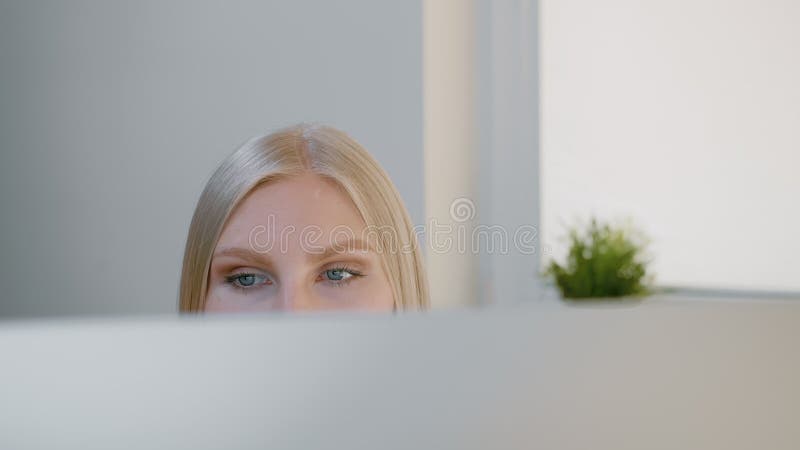 Female looking at computer monitor. Blond attractive woman sitting at window and looking attentively at computer screen