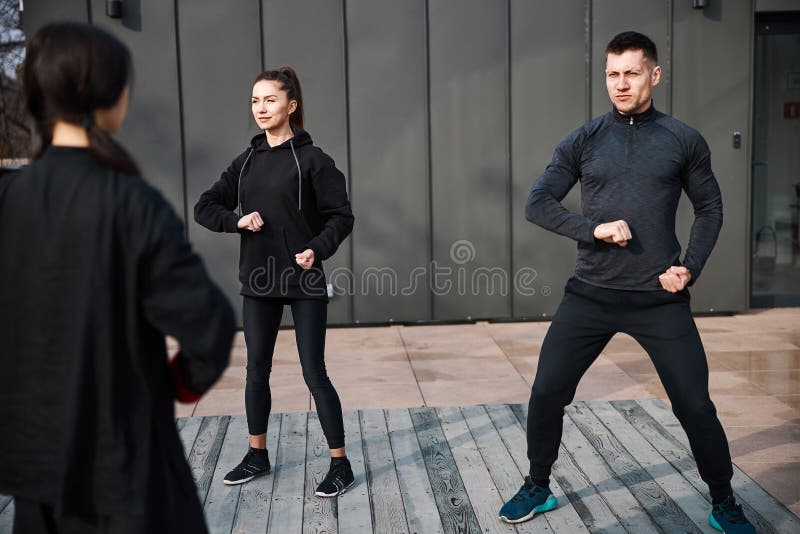 Sportive men with lady folding right arm and keeping fist before torso with left hand near waist. Qigong class stock images, royalty-free photos and pictures