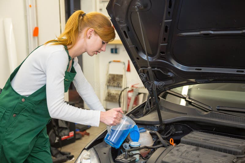 Female mechanic fills coolant or cooling fluid in motor of a car