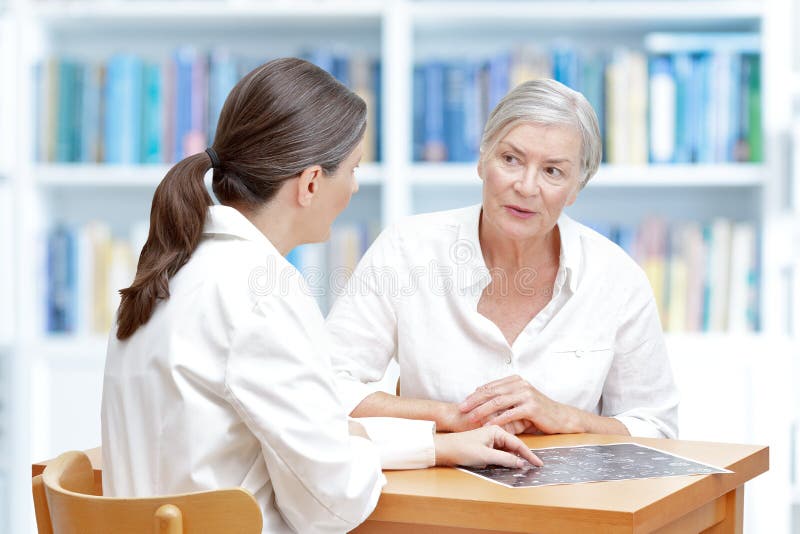 Female middle aged doctor in her surgery showing her senior stroke patient the latest ct scan of her brain. Female middle aged doctor in her surgery showing her senior stroke patient the latest ct scan of her brain