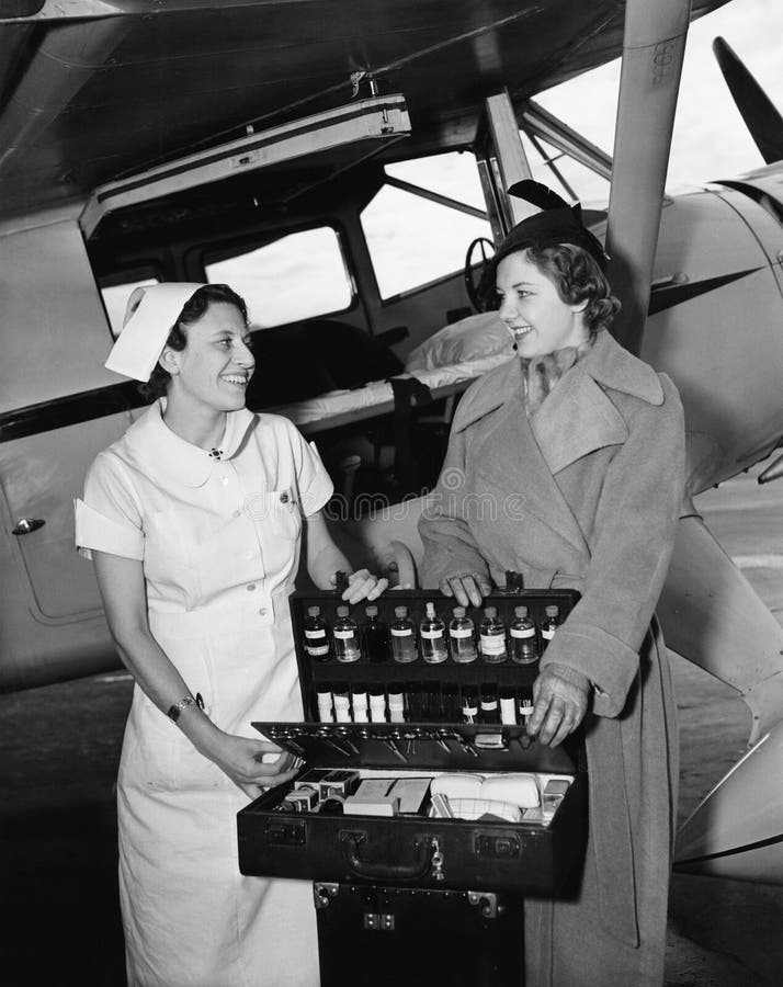 Female nurse with a young woman standing in front of an airplane and opening a medicine box (All persons depicted are no longer living and no estate exists. Supplier grants that there will be no model release issues.)