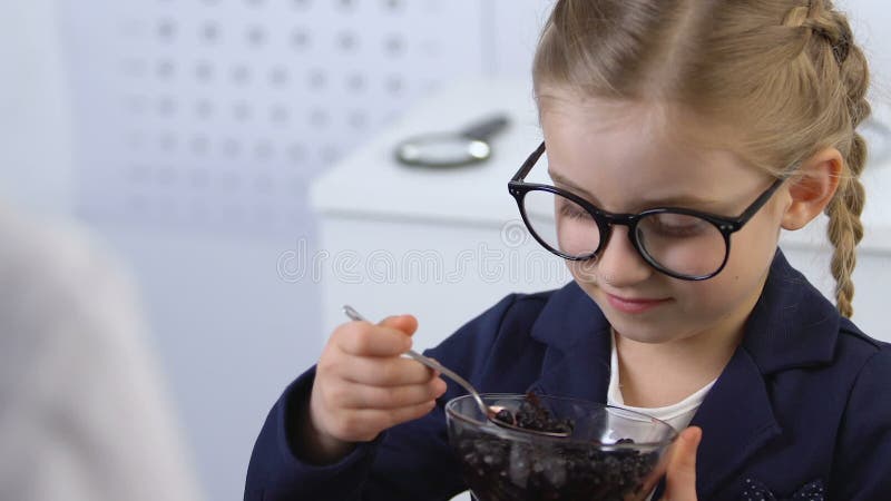 Female oculist giving blueberry bowl to kid in eyeglasses, eye health, vitamins