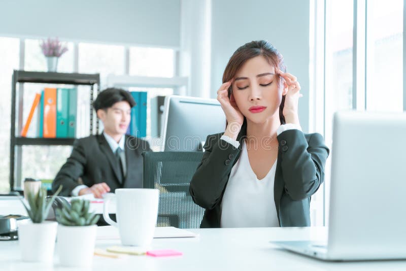 Female officer is having migraine headache after a tired day of working in front on the computer laptop in office, office syndrome royalty free stock photography