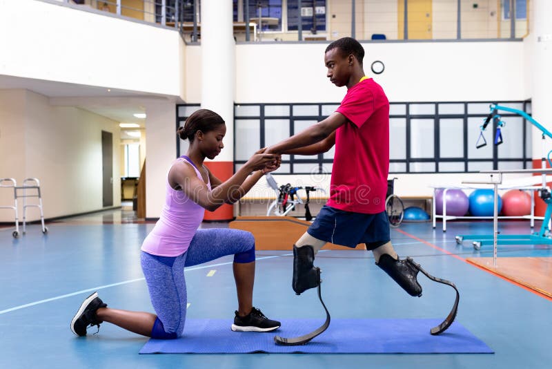 Female physiotherapist helping disabled man walk with prosthetic leg in sports center