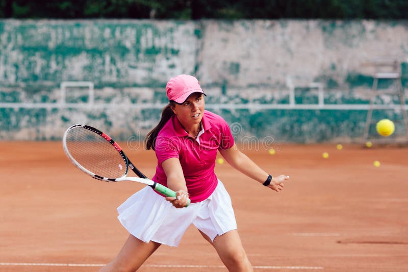 Female player dressed in pink skirt and white blouse, playing tennis on court, ready to hit a ball. In action