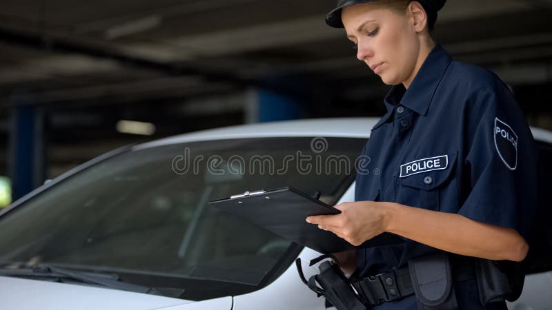 Female police officer writing traffic ticket for parking violation near car